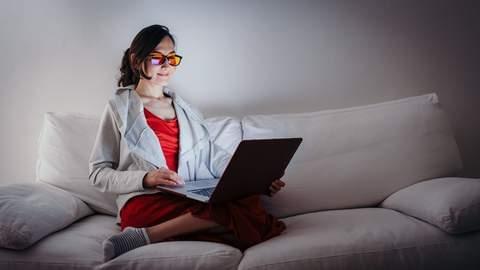 woman on a laptop on a couch smiling after being well rested